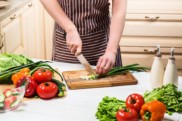 Young woman cooking in the kitchen at home. Healthy food. Diet. Dieting concept. Healthy lifestyle. Cooking at home. Prepare food. A woman cuts a green onion and vegetables with a knife.