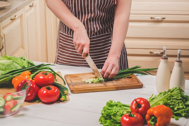 Young woman cooking in the kitchen at home. Healthy food. Diet. Dieting concept. Healthy lifestyle. Cooking at home. Prepare food. A woman cuts a green onion and vegetables with a knife.