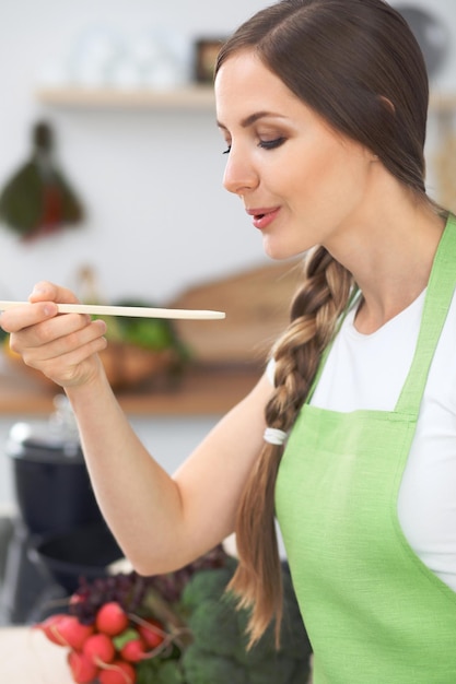 Young woman cooking in a kitchen Housewife tasting soup by wooden spoon