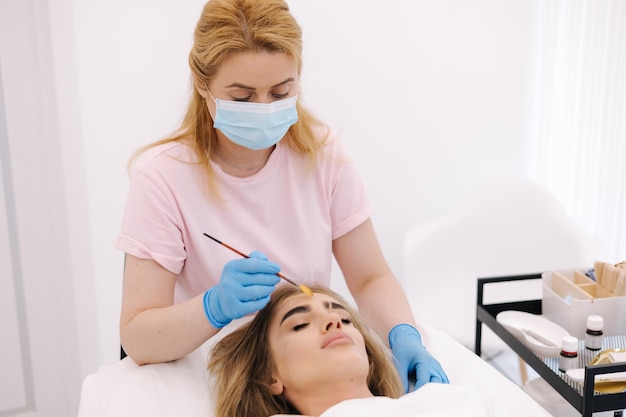 Young woman cosmetologist apply white clay mask on womans face beautiful woman in beauty salon