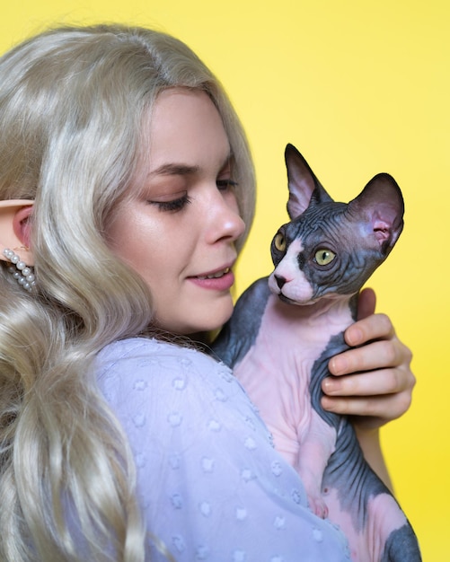 Young woman cosplay elf in blue dress holds Sphinx kitten in hands looking at it with love