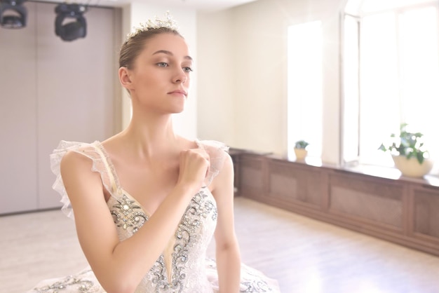 A young woman in a creamcolored dress wearing a crown is putting on her makeup in front of the mirror The concept of beauty