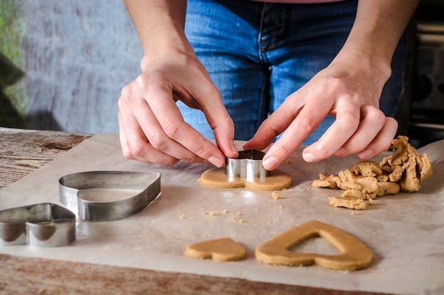 A young woman cuts figurines from a dough with logs on a wooden table