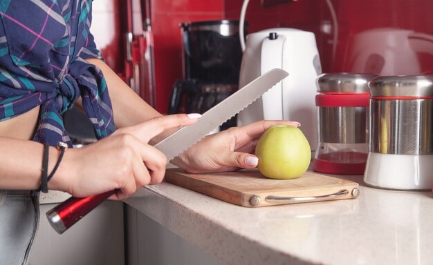 Young woman cuts fresh apple on wooden board.