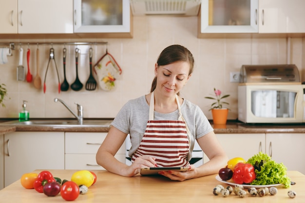 The young woman cuts vegetables in the kitchen with a knife and laptop on the table. Vegetable Salad. Dieting Concept. Healthy Lifestyle. Cooking At Home. Prepare Food.