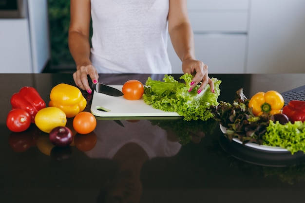 The young woman cuts vegetables in the kitchen with a knife