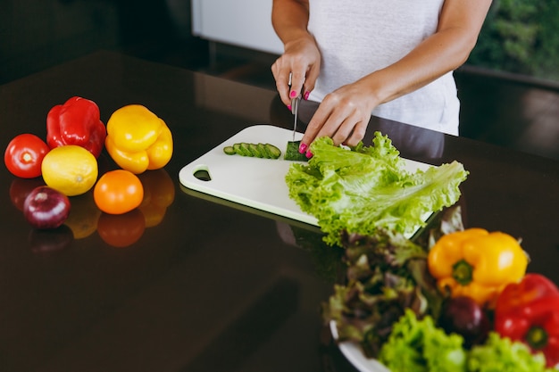 The young woman cuts vegetables in the kitchen with a knife