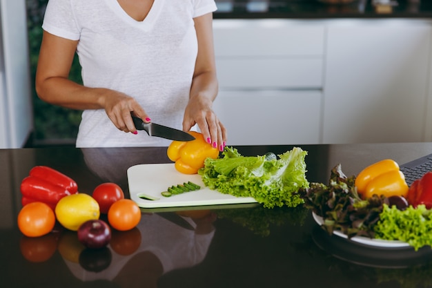 The young woman cuts vegetables in the kitchen with a knife