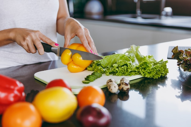 The young woman cuts vegetables in the kitchen with a knife