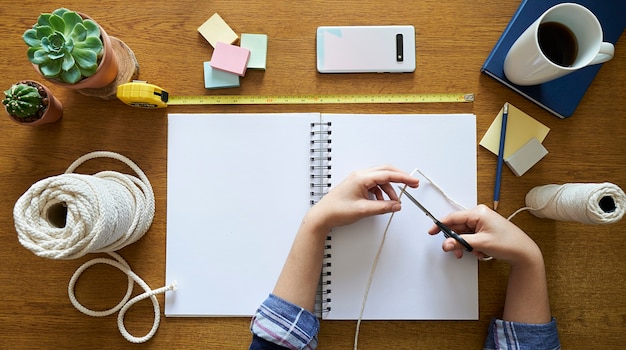 young woman cutting macrame with scissors to create a handmade decor on a wooden desk