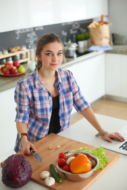 Young woman cutting vegetables in kitchen near desk