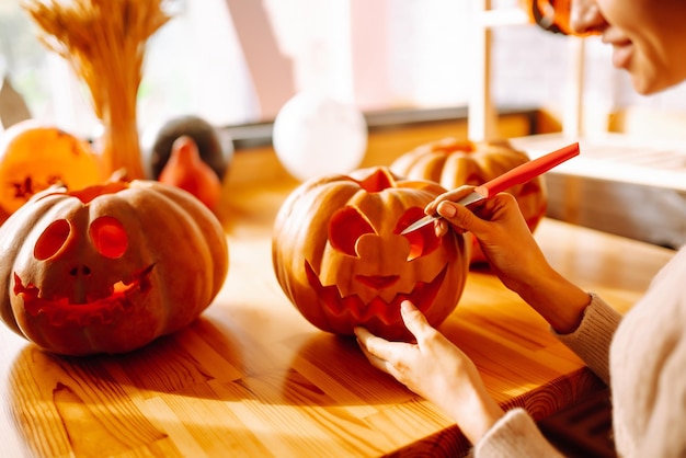 Young woman cutting with knife character face on pumpkin object preparation to halloween holiday