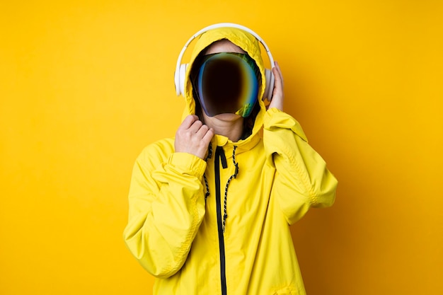 Young woman in cyberpunk glasses with headphones in a yellow jacket on a yellow background