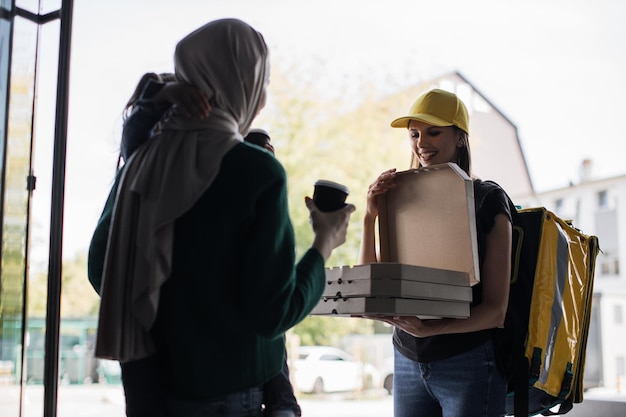 Young woman delivery pizza to beautiful muslim girl customer with a little cute daughter