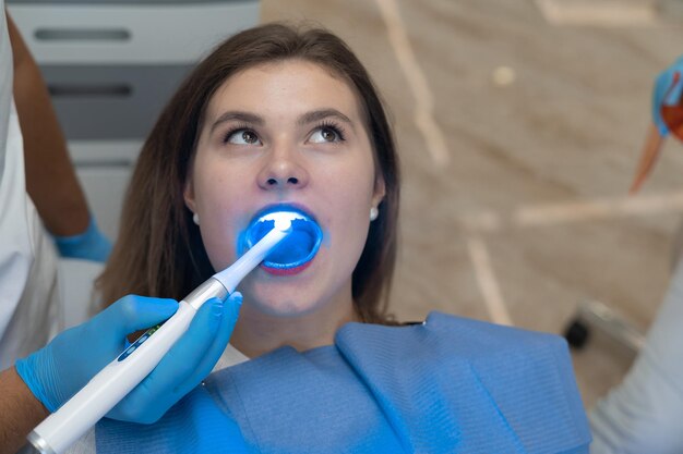 Young woman at the dentist appointment. The mouth is wide open. Look for caries using ultraviolet light.