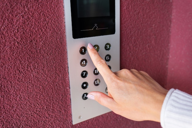 A young woman dials the apartment code on the panel of an electronic intercom. Protection and safety concept.