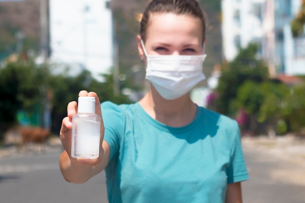 Young woman disinfects hands, girl in protective medical mask on face show bottle with sanitizer