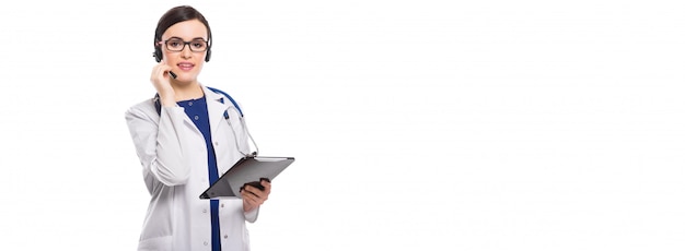 Young woman doctor with stethoscope and headphones holding tablet in her hands in white uniform