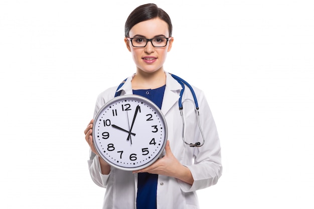 Young woman doctor with stethoscope holding clock in her hands in white uniform on white 