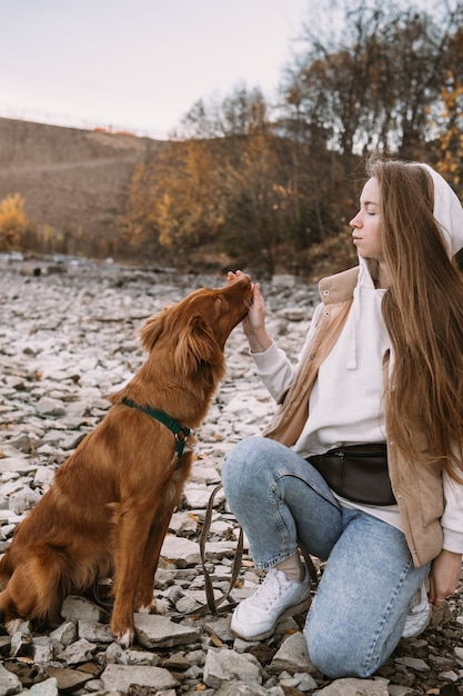 Young woman and dog retriever walks on river shore at autumn season