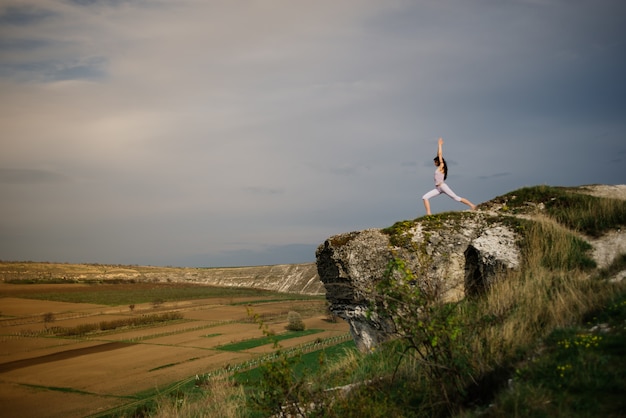 Young woman doing complex Yoga exercise on a rock