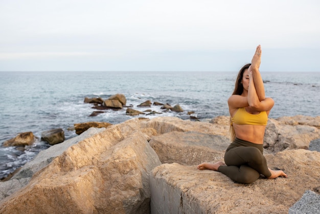 Young woman doing gomukhasana with garudasana arms Yoga practice in nature near the oceanCopy space Healthy lifestyle and spirituality concept