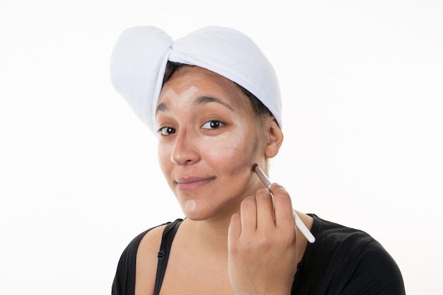 Young woman doing her makeup with a towel on her hair