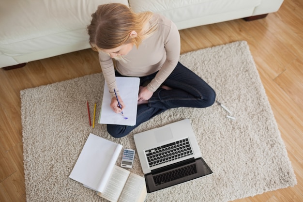 Young woman doing homework and sitting on floor using laptop