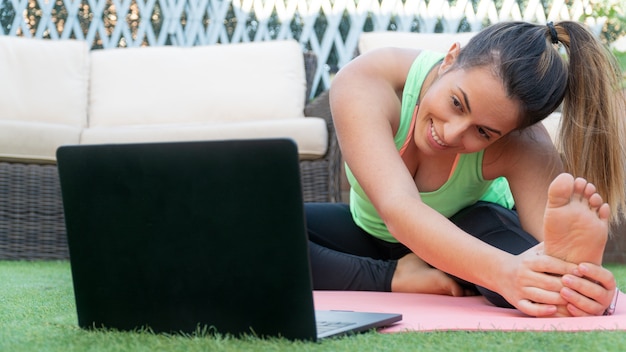 Young woman doing an online yoga class in her garden