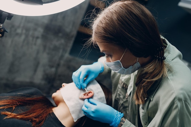 Young woman doing piercing at beauty studio salon