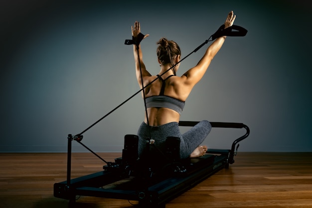 Young woman doing pilates exercises with a reformer bed. Beautiful slim fitness trainer. Fitness concept