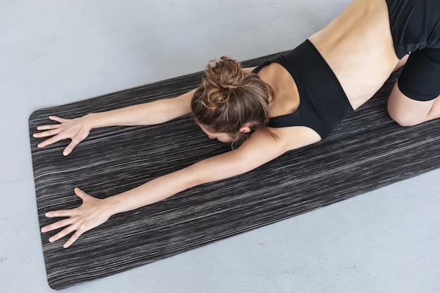 Young woman doing a variation of ashtanga namaskarasana exercise working out in black sportswear