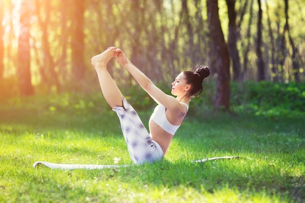 Young woman doing yoga exercises in the summer city park health lifestyle concept