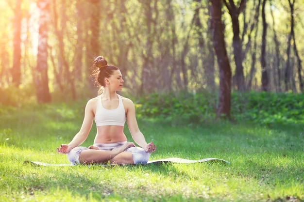 Young woman doing yoga exercises in the summer city park health lifestyle concept