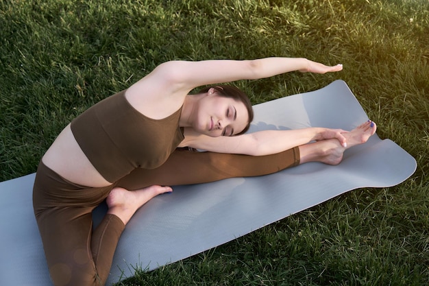 Young woman doing yoga lying on a mat in the park