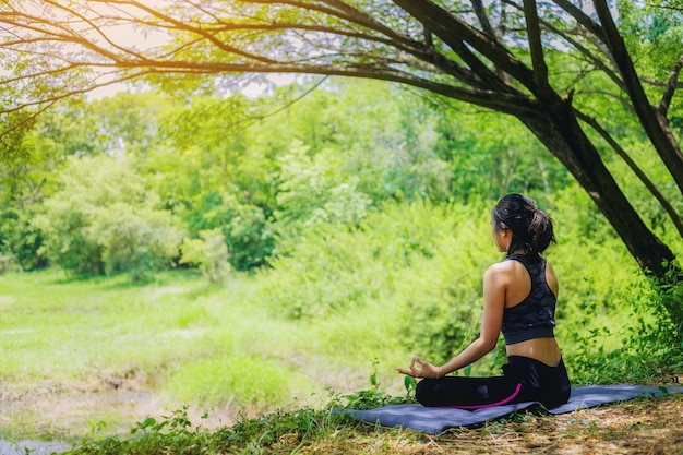 Young woman doing yoga pose under the tree close the nature