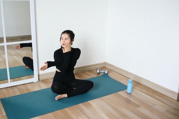 Young Woman Doing Yoga Stretching Arms While Sitting On Exercise Mat At Home