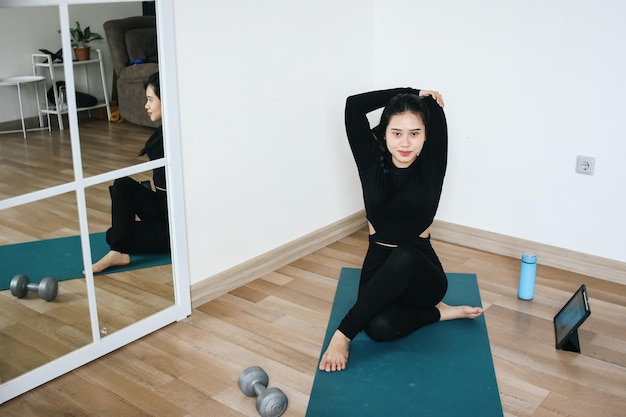 Young Woman Doing Yoga Stretching While Sitting On Exercise Mat At Home