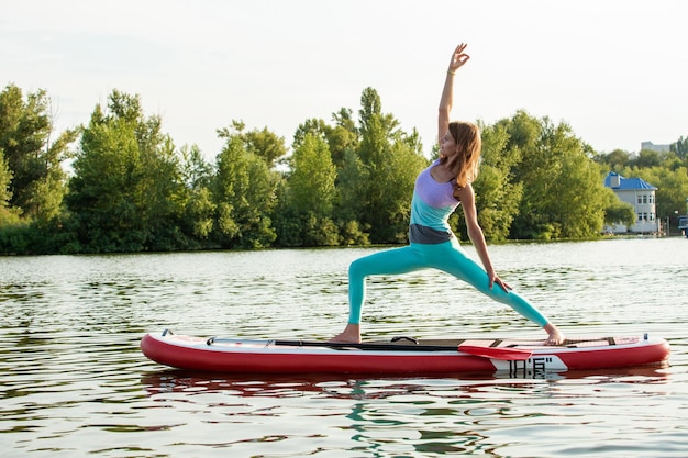 Young woman doing yoga on sup board with paddle yoga pose side view  concept of harmony with the nature