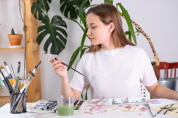 A young woman draws with gouache on a white sheet. Meditation drawing. A woman chooses a suitable br