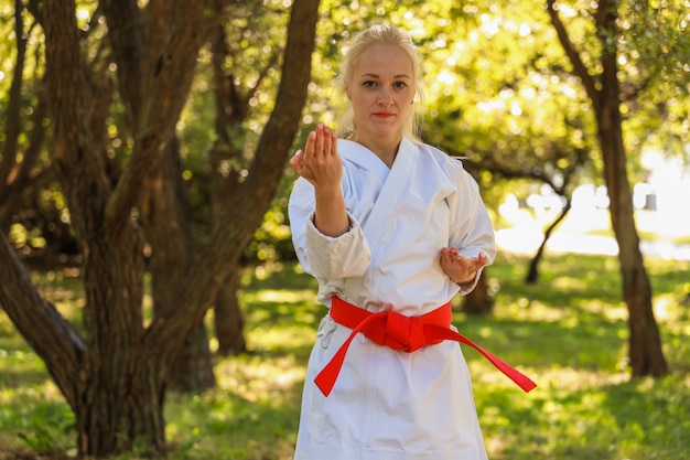 Young Woman Dressed In Kimono Practicing Her Karate Moves in park - red belt