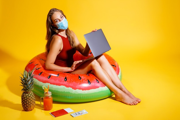 Photo young woman dressed in red swimsuit sitting on inflatable circle on the yellow backgroundwearing a m...