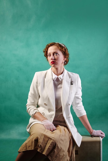 Young woman dressed in retro style sitting on a suitcase. Studio shot