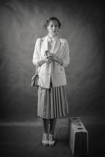 Young woman, dressed in retro style, with a suitcase and a book in her hands. Studio portrait