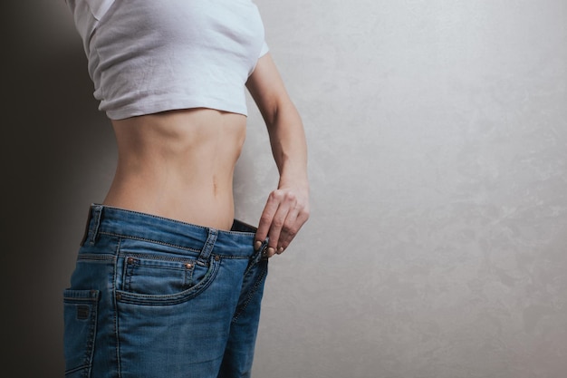 Young woman dressed in wide jeans and a white shirt demonstrates successful weight loss concept of