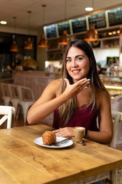 Young woman drinking coffee, making the sign of a listener.