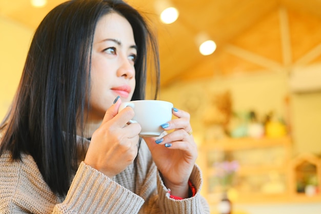 Young woman drinking coffee or tea relaxed woman smelling coffee at home in winter with cup coffee woman coffee with hand holding a cup in cafe