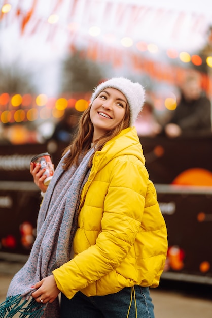 Young woman drinking hot coffee while walking near New year tree.