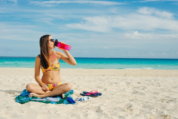 Young woman drinking sparkling water from transparent bottle on the beach cancun