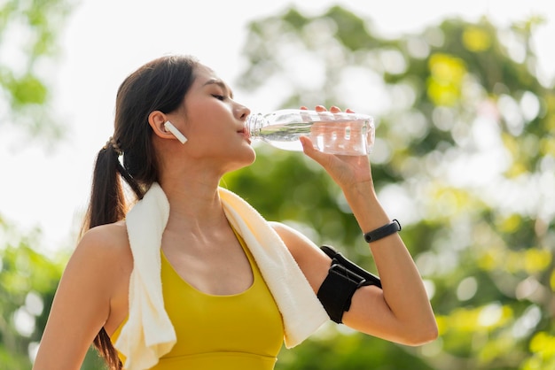 Young Woman drinking water from bottle asian female drinking water after exercises or sport Beautiful fitness athlete woman wearing hat drinking water after work out exercising on sunset evening